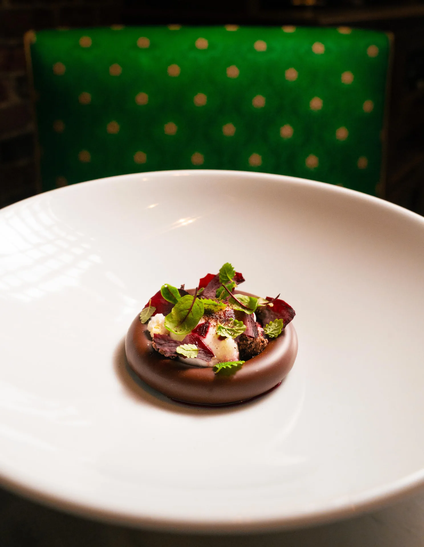 A plated dessert with green herbs and red petals in a white bowl