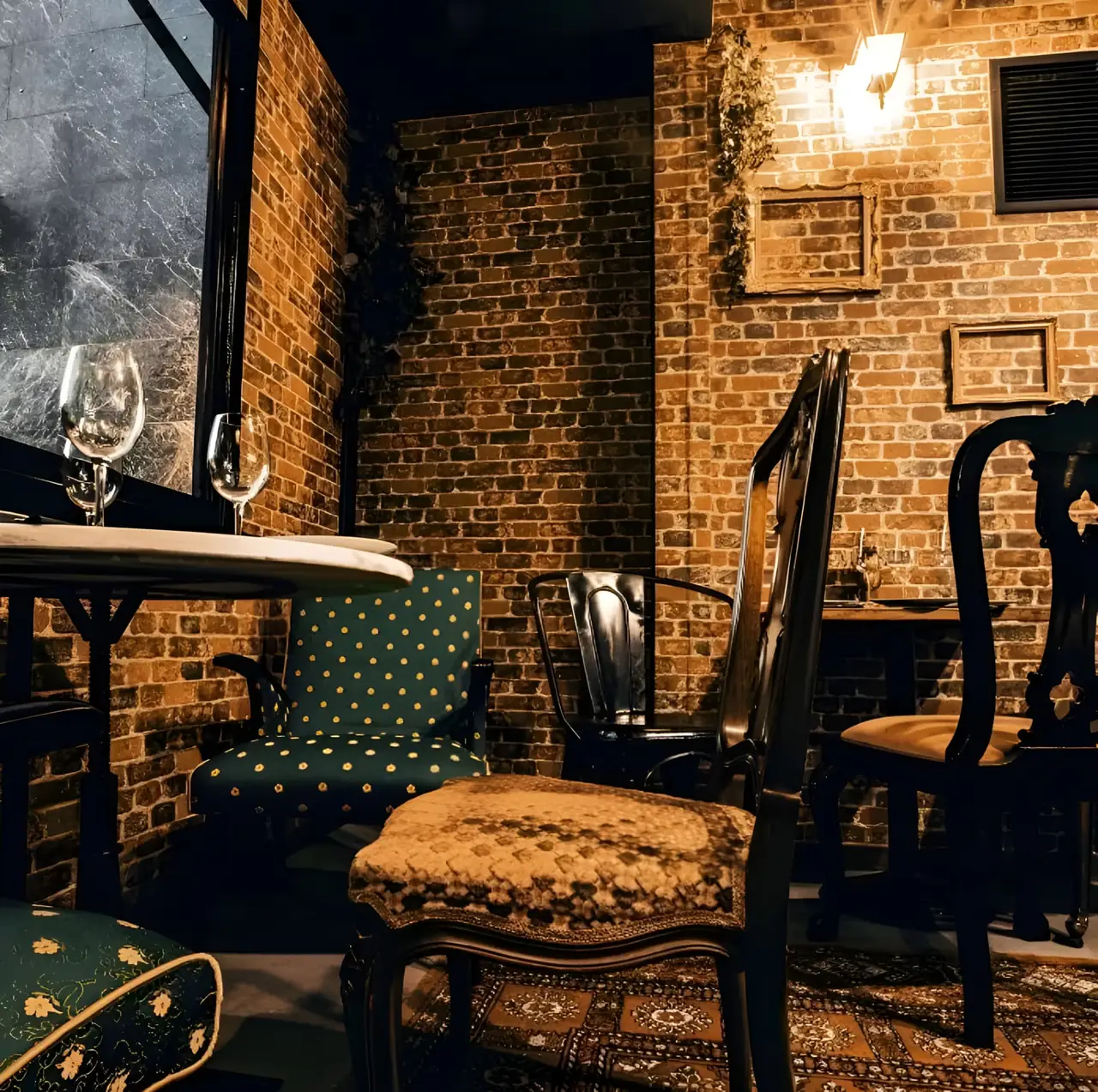 A marble table set with wine glasses against a candlelit brick wall
