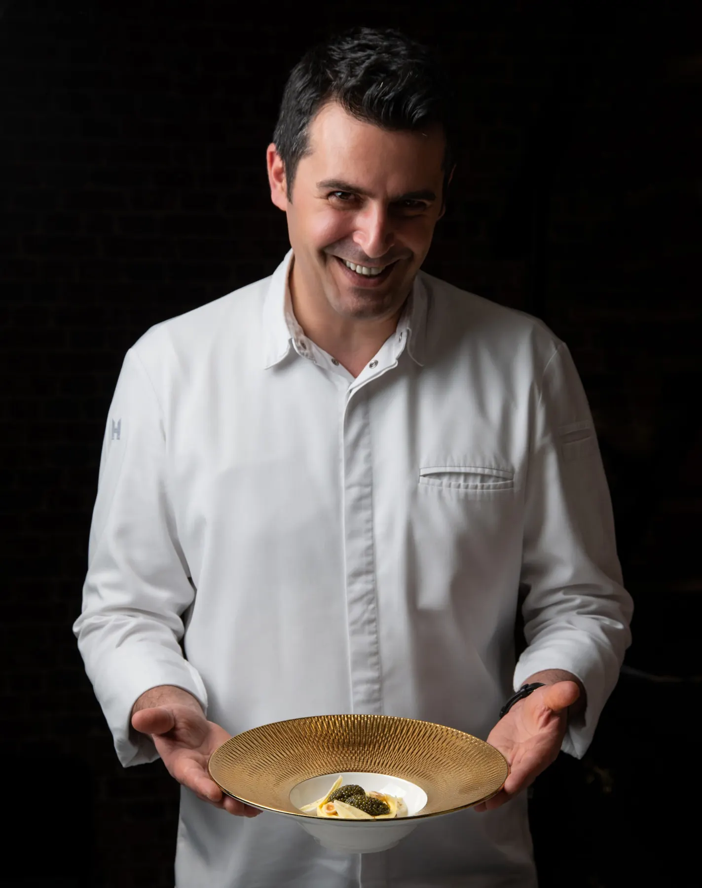 Chef Panagiotis Polychronis looking down at a plated dessert on the marble counter