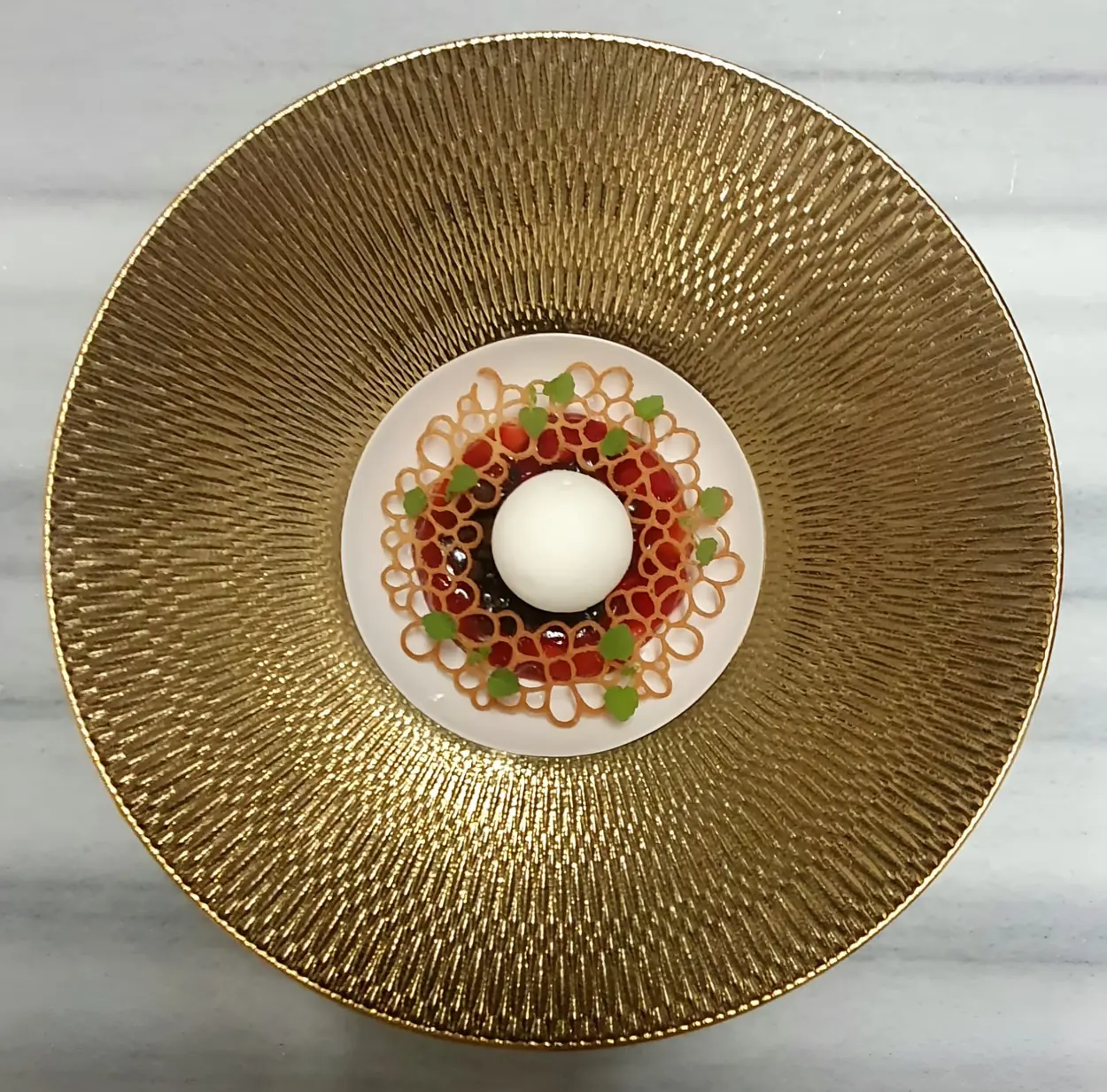 Overhead view of a gold-ridged plate with a white dome and red beads